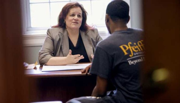 woman talking to male student at desk