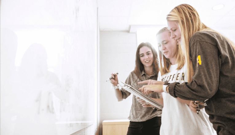 3 students writing on whiteboard and talking