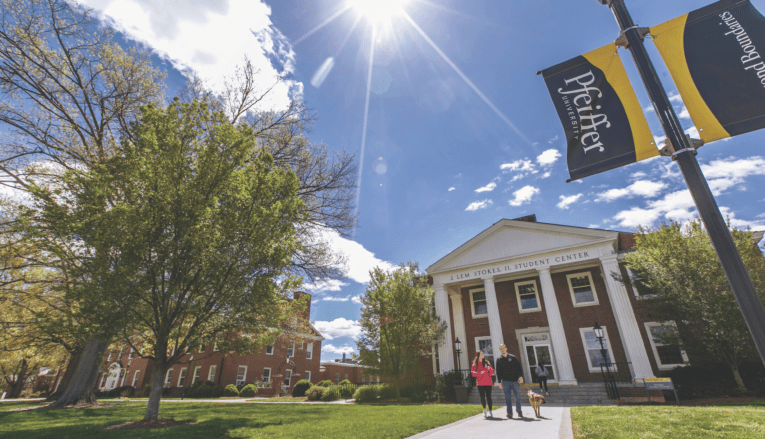 blue sky shining on pfeiffer building with students walking dog