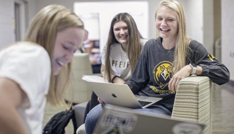 3 students smiling and sitting while on laptops