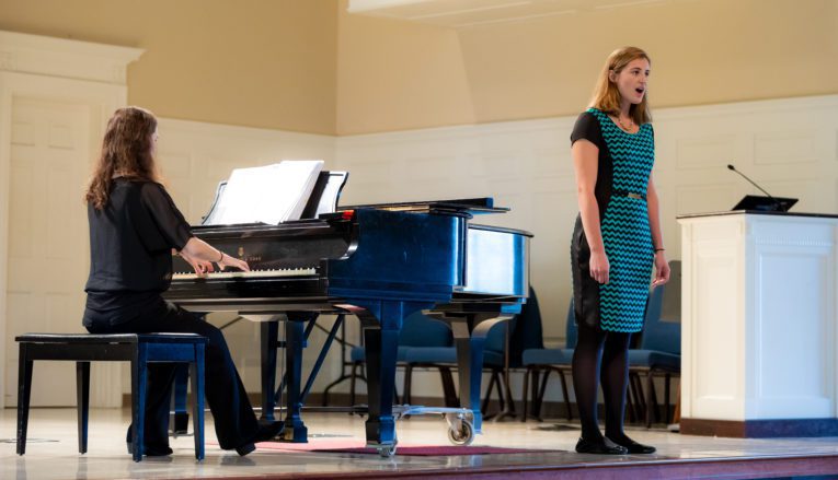 Two students performing on stage, one singing and on playing piano