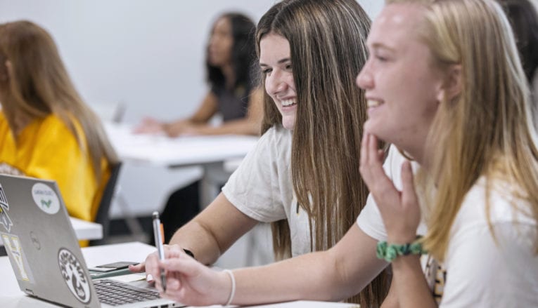 Two students smiling in class with laptop