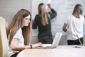 two women writing on white board while another woman is on a laptop