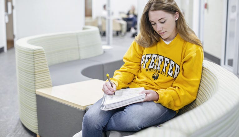 Student sitting on couch writing in notebook
