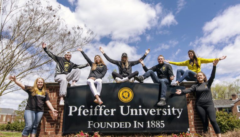 Group of students sitting around Pfeiffer campus sign