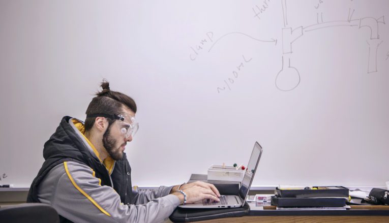 male student wearing safety glasses using computer