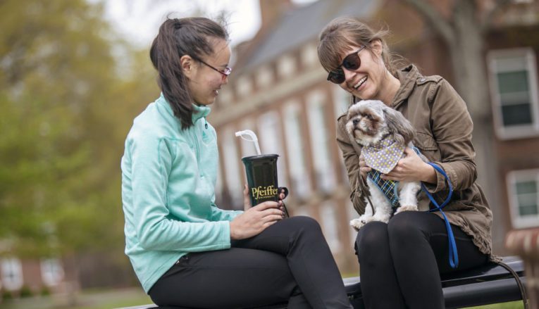 Two students sitting outside with dog