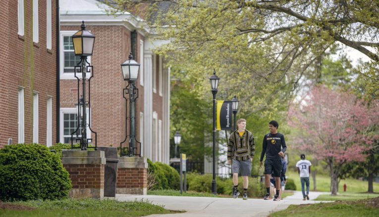 two students walking on sidewalk outside, talking and smiling