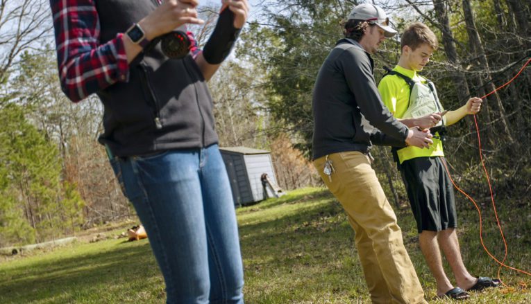 Three students outside holding fishing poles