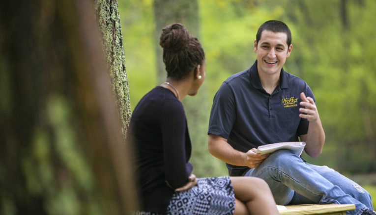 Two students sitting outside on a bench talking and studying