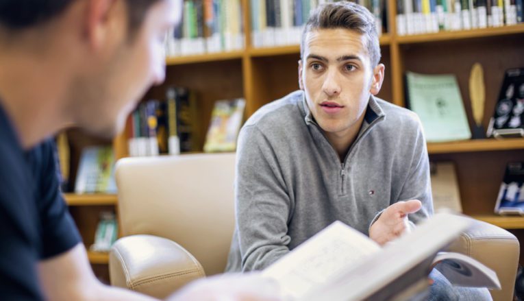 Two students talking in library holding books