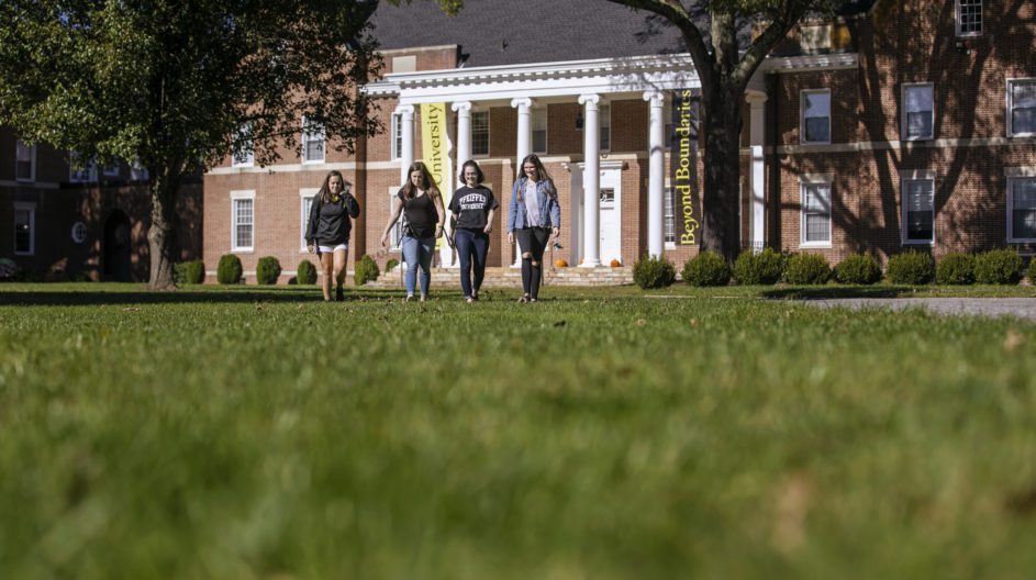 Group of students walking across campus lawn